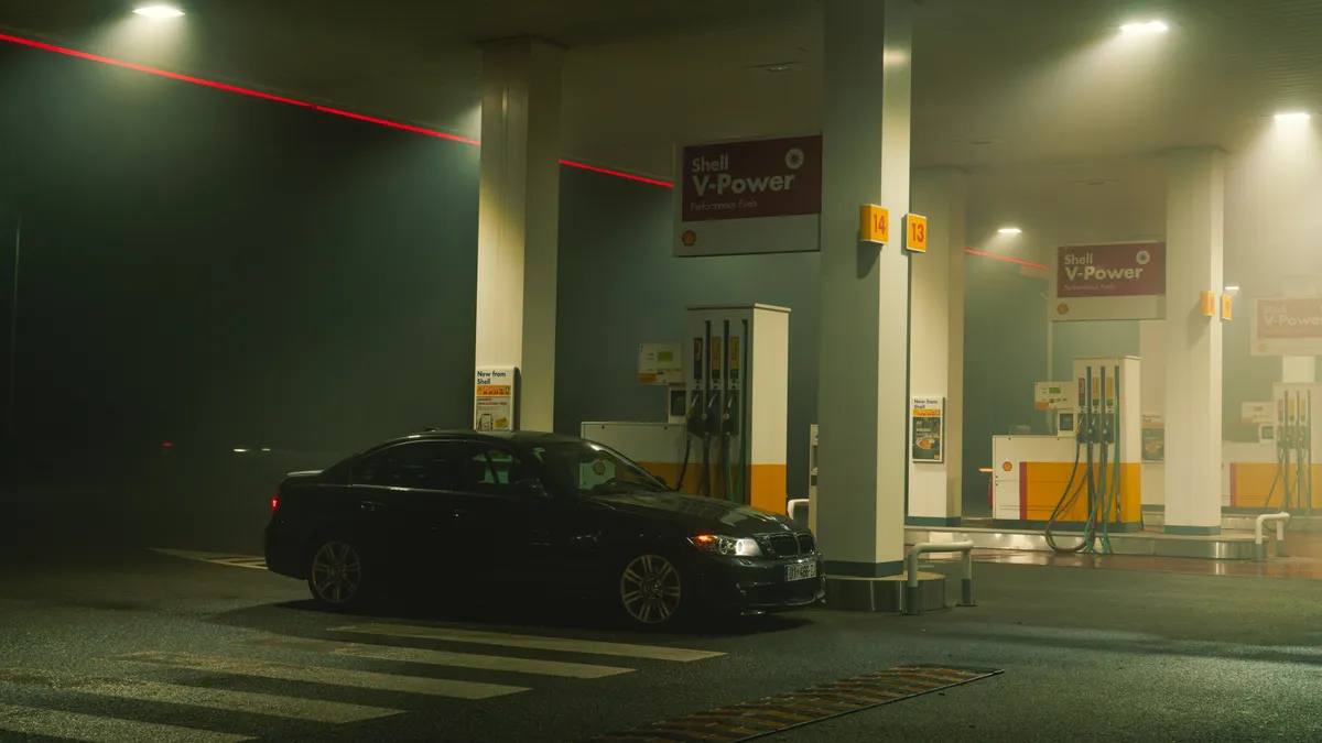 A BMW sports car parked at a Shell gas station at night, featuring bright lights and an urban setting.