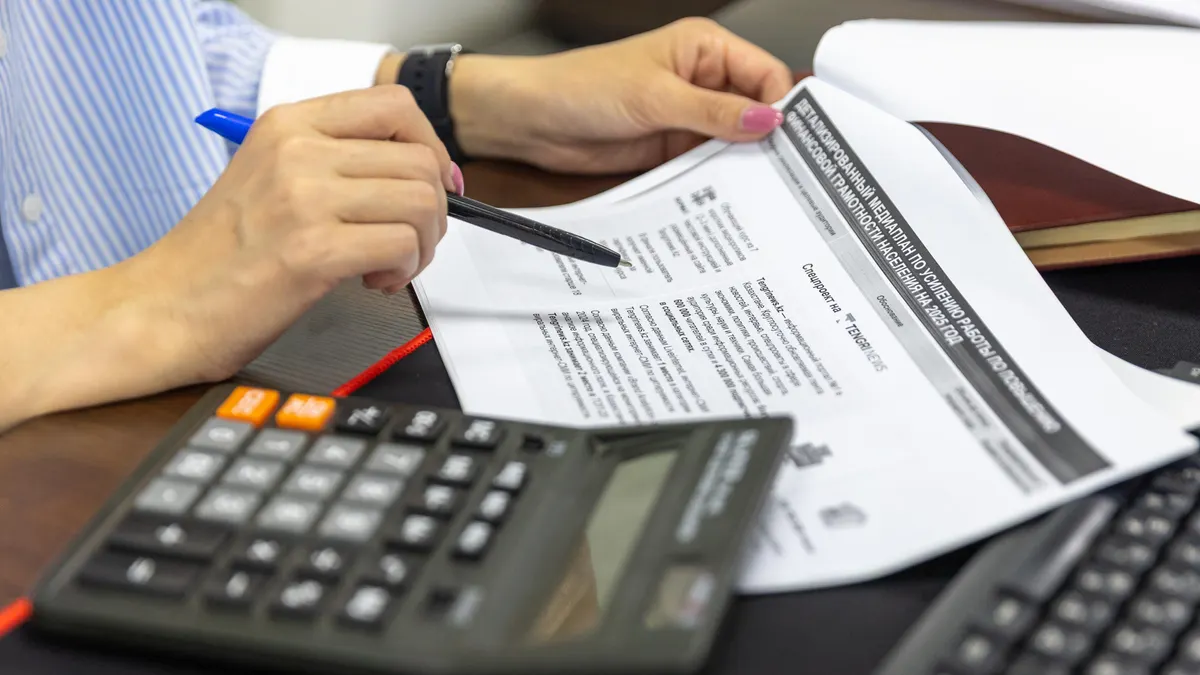 Close-up of a person analyzing financial documents using a calculator and pen.