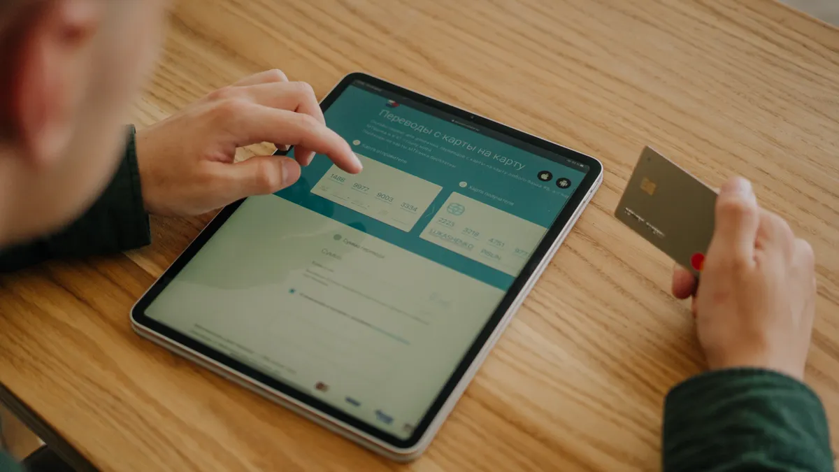 Person making an online payment using a tablet and credit card on a wooden desk.