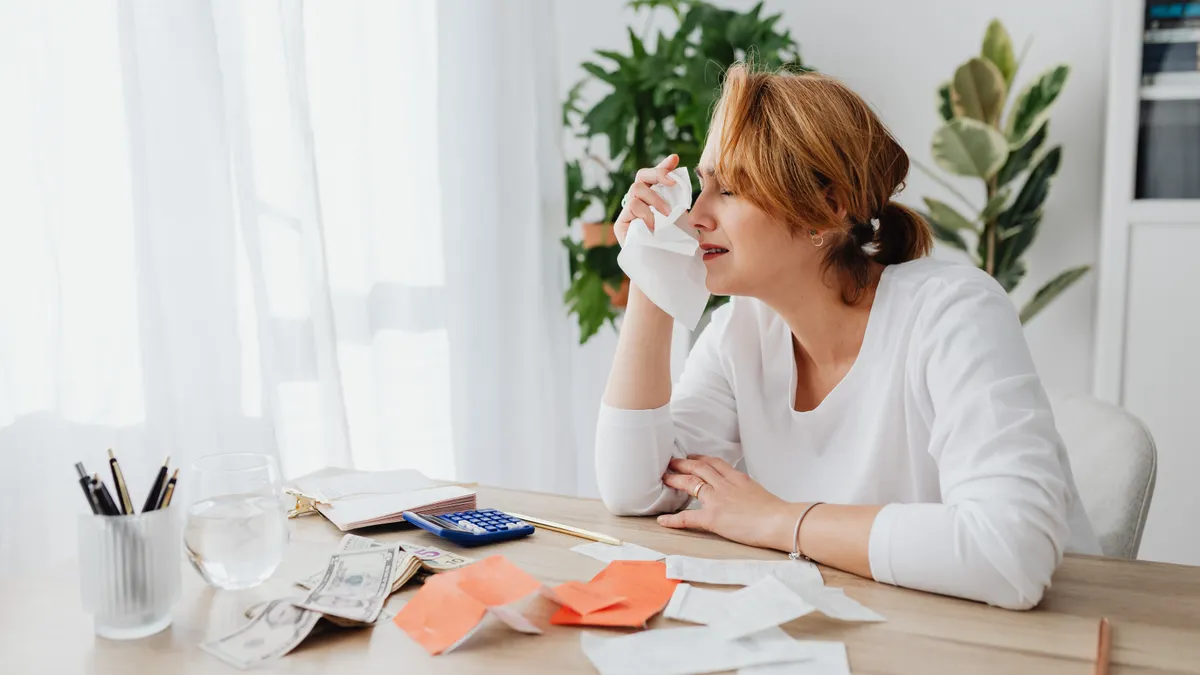 A woman is overwhelmed by bills and finances, sitting at a desk indoors.