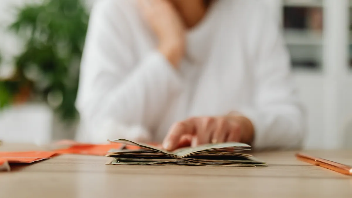 A woman sitting at a desk sorting through cash, focusing on household budgeting.