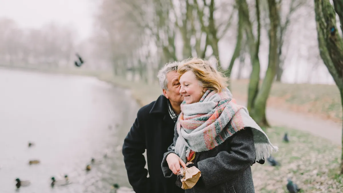 A senior couple walking by the lake, sharing a romantic moment in winter.