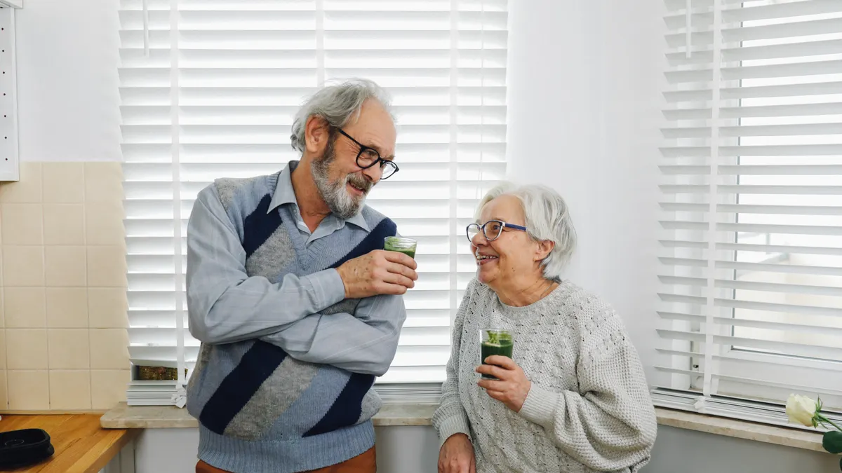 Senior couple smiling and enjoying green smoothies in a cozy kitchen setting.