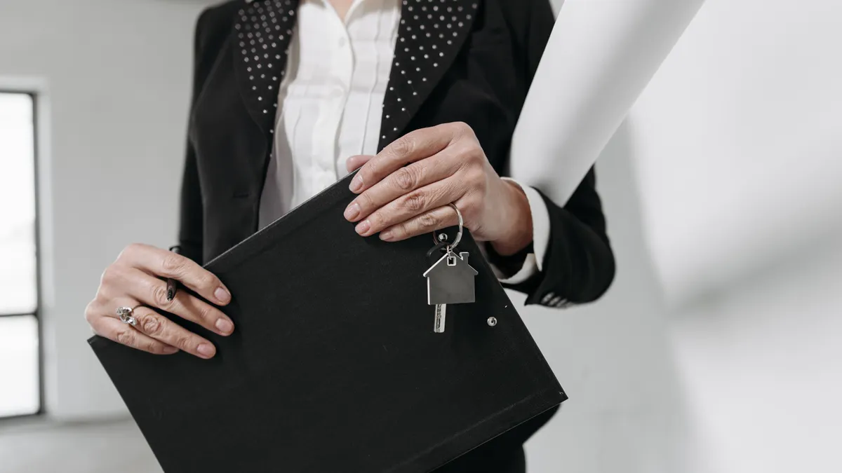 Close-up of a realtor holding a keychain and clipboard with interior office background.