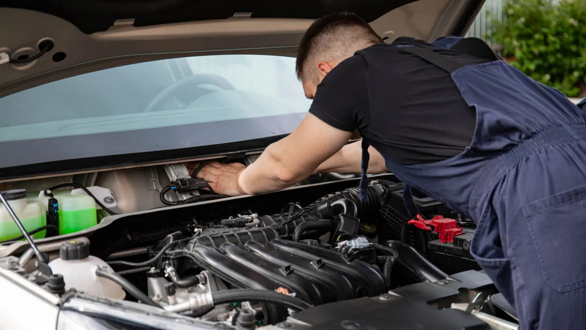Auto mechanic performs engine maintenance on a car. Focus on hands and engine components.