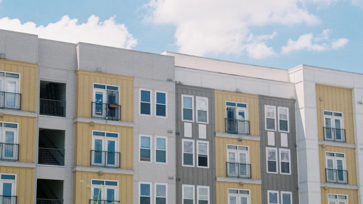Contemporary apartment building exterior with yellow and grey panels under a clear blue sky.