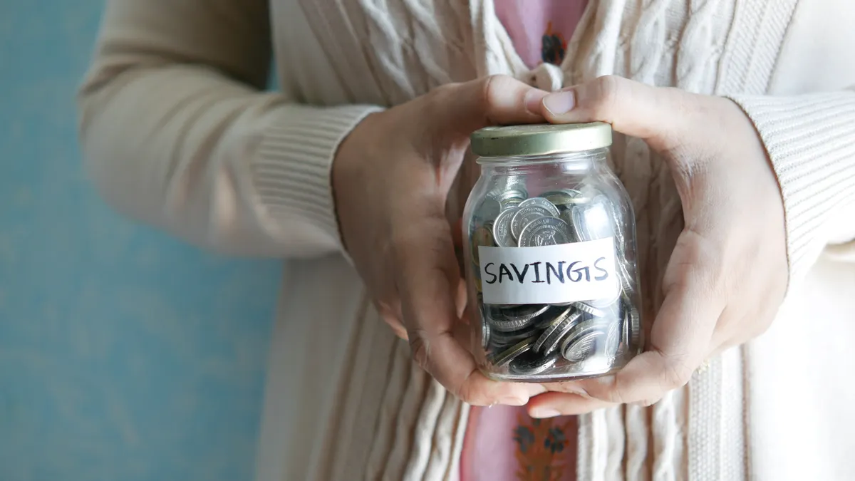 Woman holding a jar labeled 'savings' filled with coins, representing financial savings.